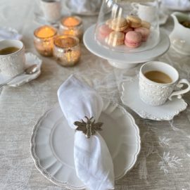 gedeckter Kaffeetisch mit Tischdecke aus französischem Leinen natur mit weißen floralen Motiven und Vögeln und weiße Leinenservietten mit französischem Flair