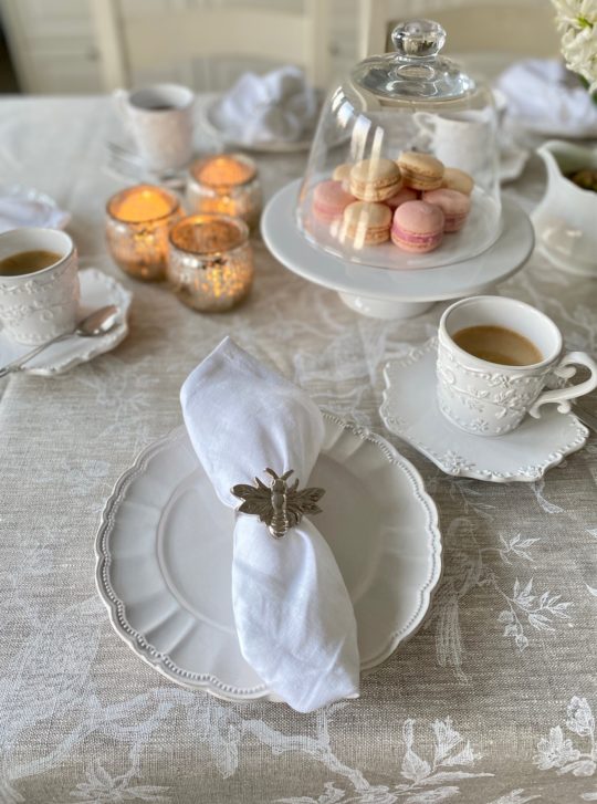 gedeckter Kaffeetisch mit Tischdecke aus französischem Leinen natur mit weißen floralen Motiven und Vögeln und weiße Leinenservietten mit französischem Flair